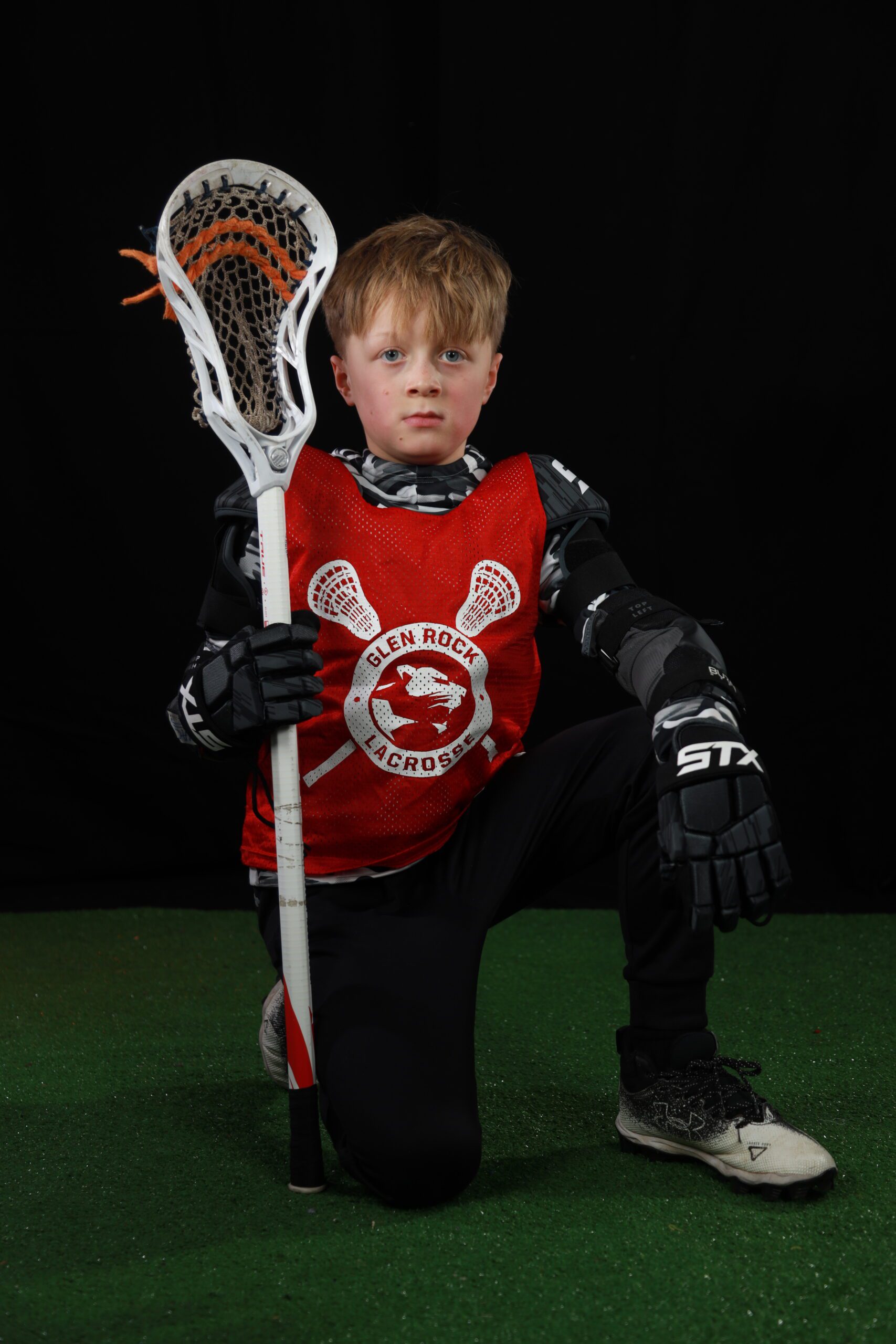 Posing with a lacrosse stick in an indoor sports photography setting.