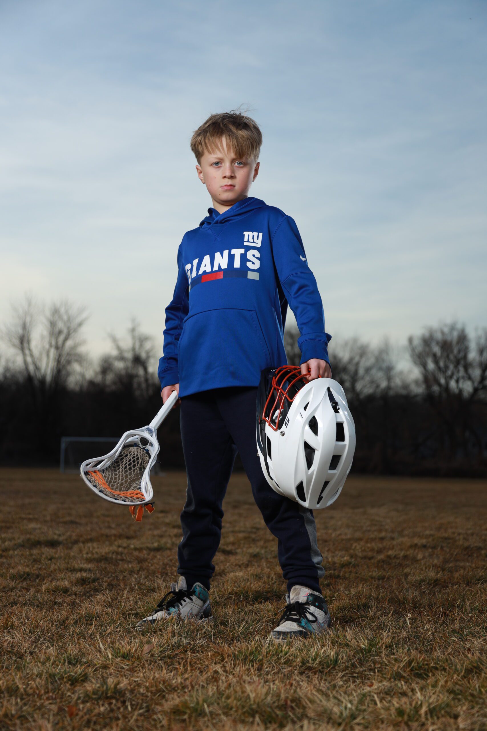 Posing with a lacrosse stick and helmet in outdoor sports photography sessions.