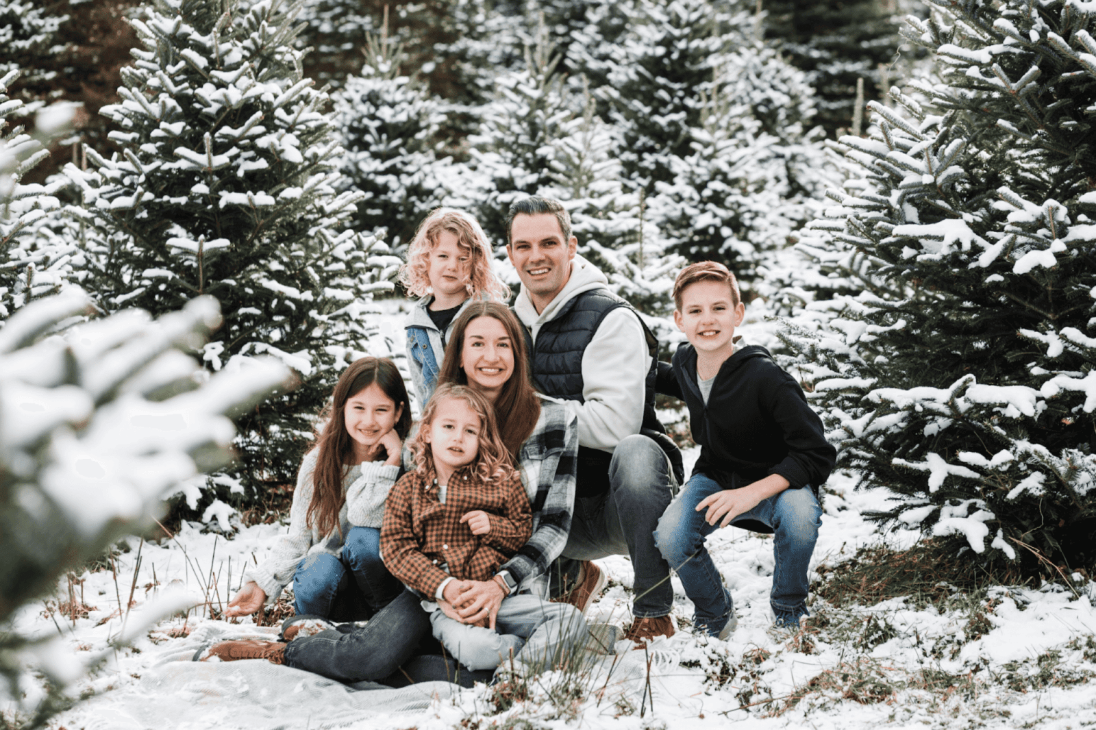 Family posing outside in front of trees in the snow during the holidays