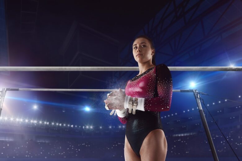 gymnast with pink and black leotard clapping hand chalk and uneven bars in the background