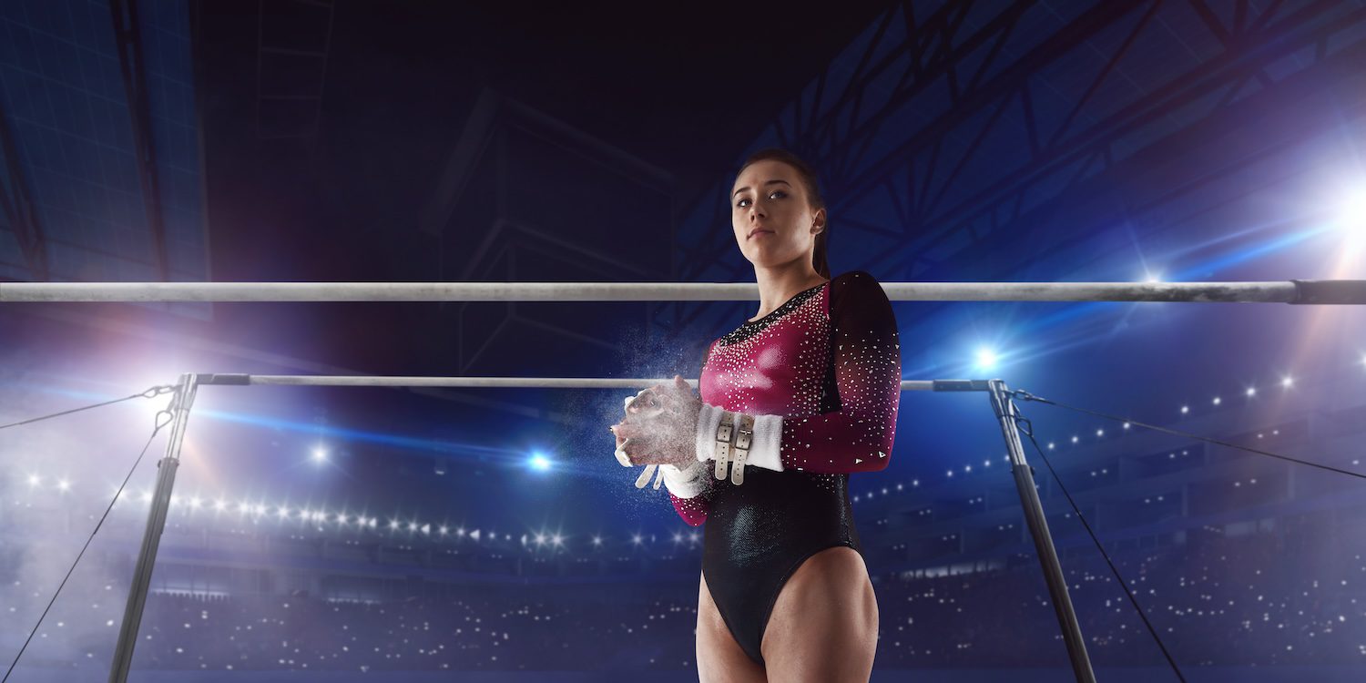 gymnast with pink and black leotard clapping hand chalk and uneven bars in the background