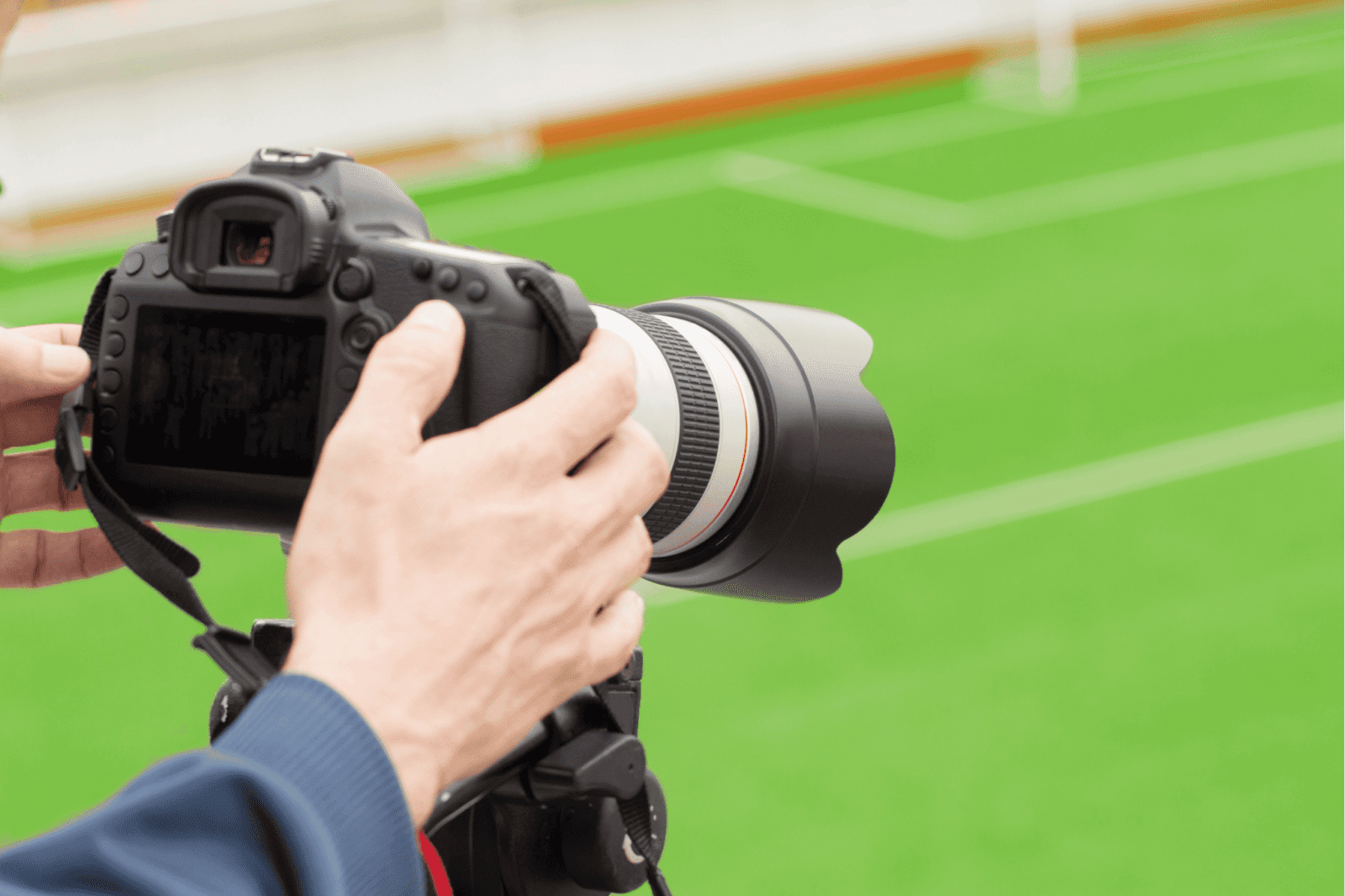 A sports photographer holds a camera on a soccer field