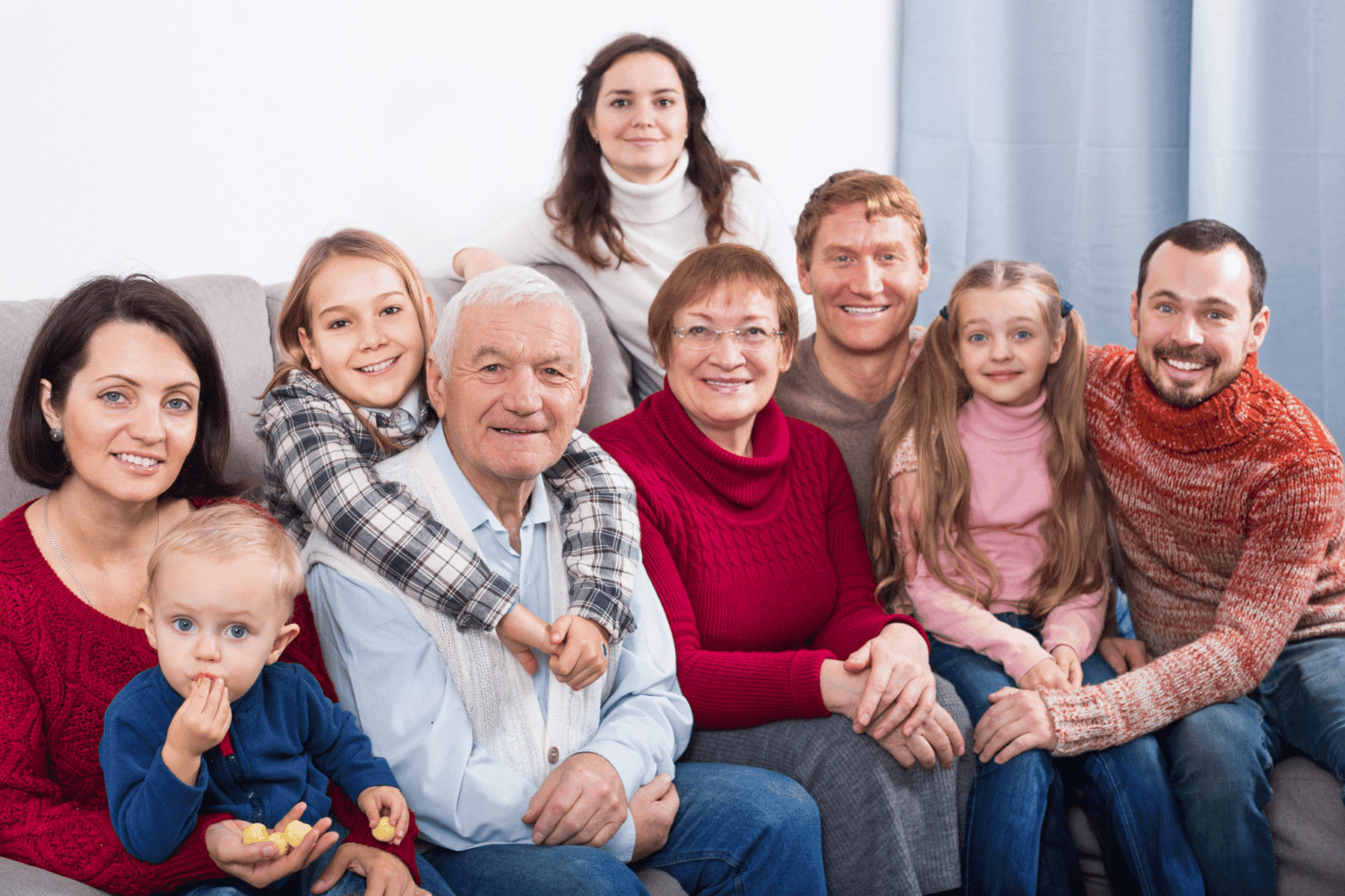 A family of parents, grandparents, and children poses inside on a couch