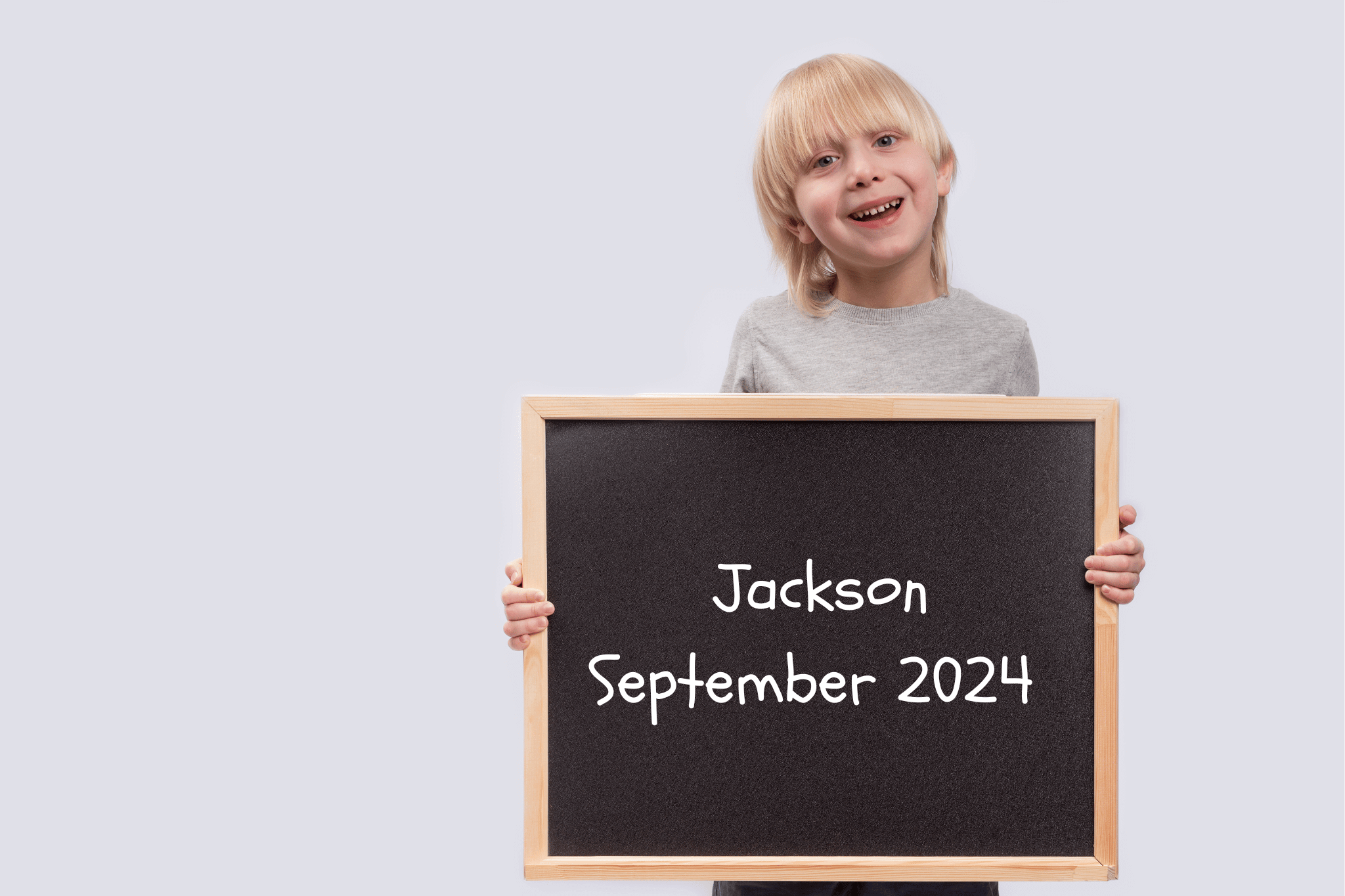 A kindergarten child holds a chalkboard showing his name and the dates